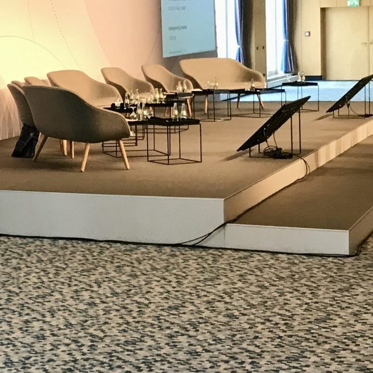 Bühne mit modernen Sesseln und Tischen, bereit für eine Veranstaltung.